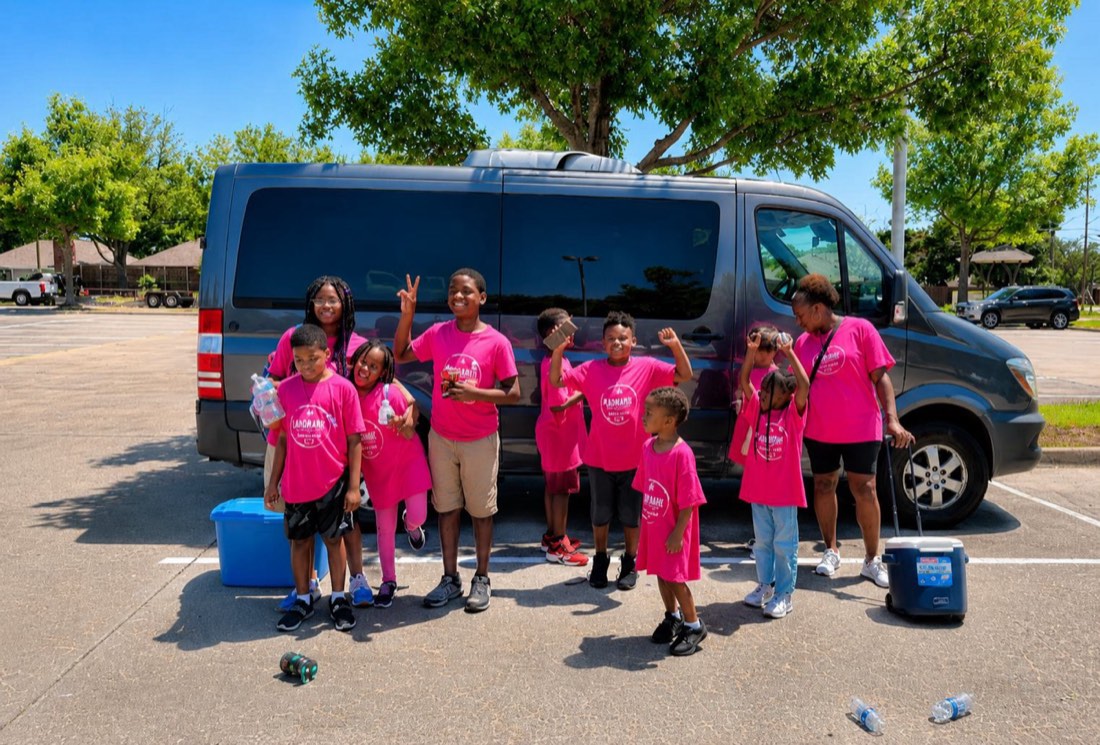A group of campers in matching pink Blackmon shirts posing by the camp van