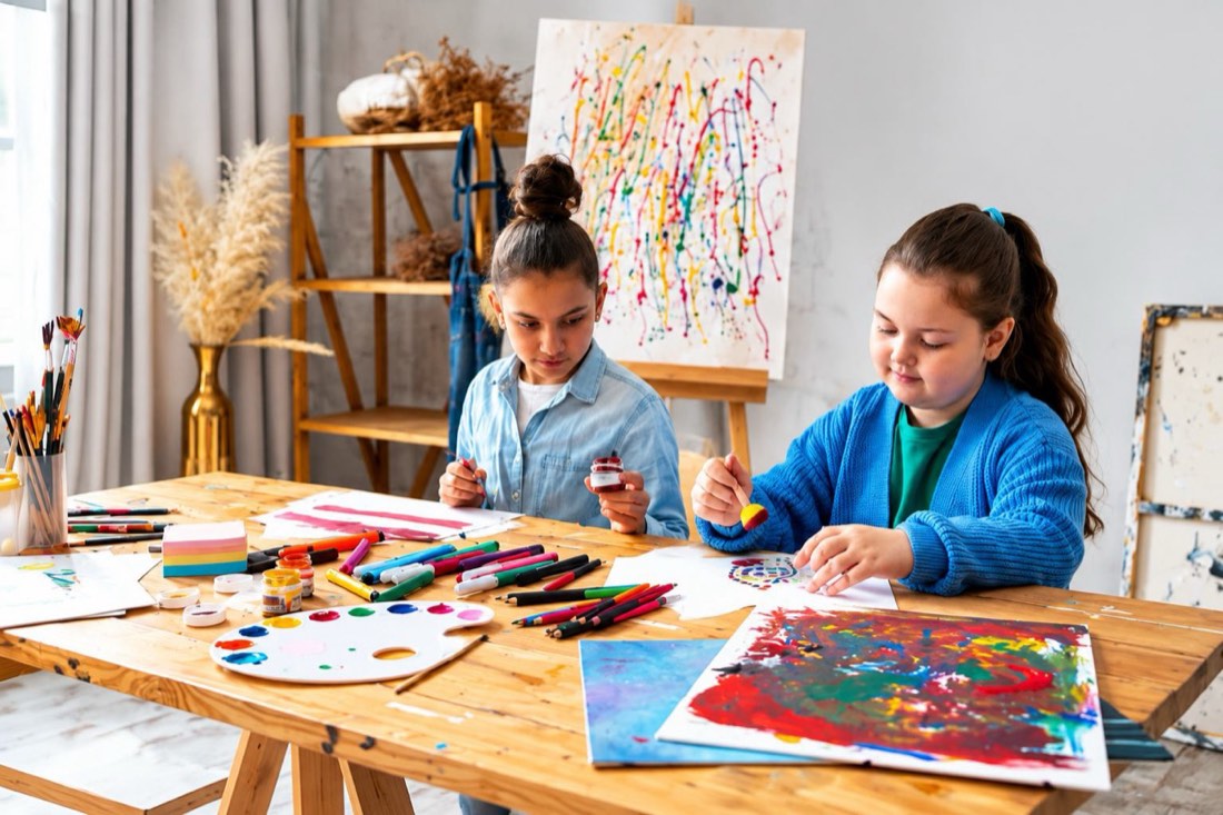 Two campers painting at an easel with colorful artwork