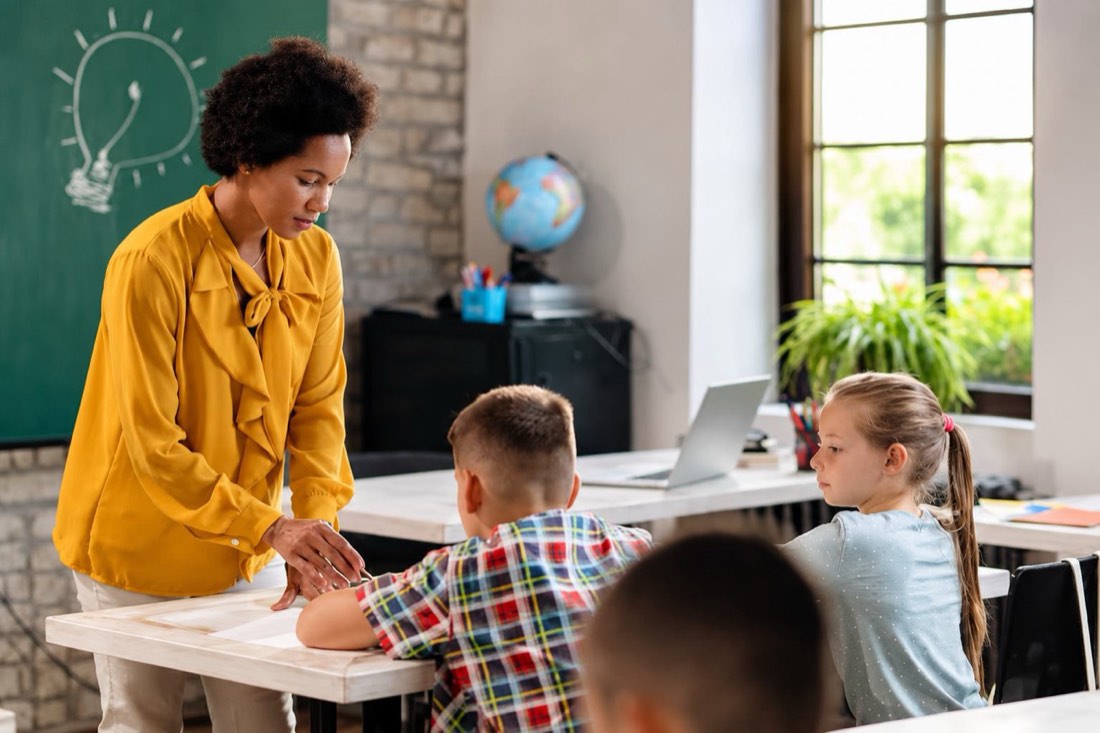 A teacher helping two students at their classroom desk