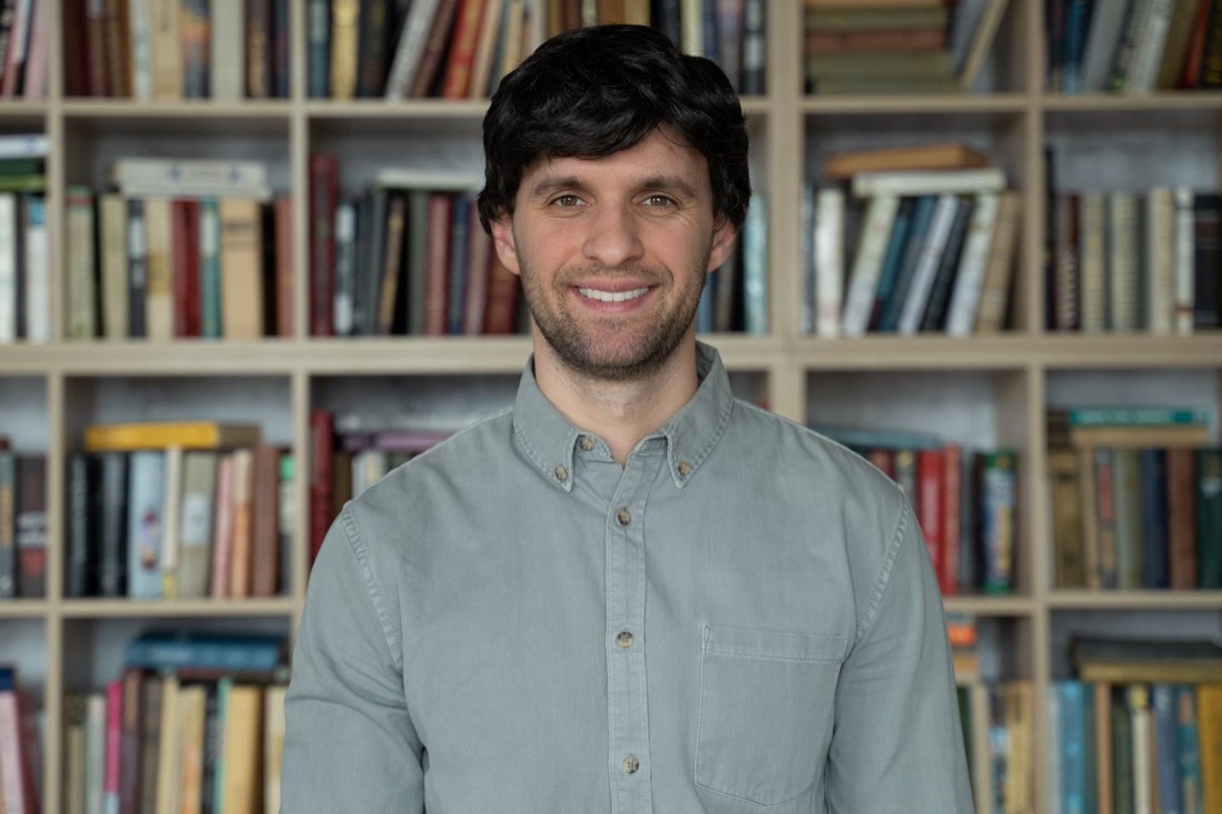 A tutor smiling in front of a bookshelf